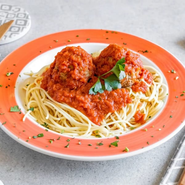 Spaghetti with two large meatballs and red sauce, garnished with parsley, on a white and orange plate.