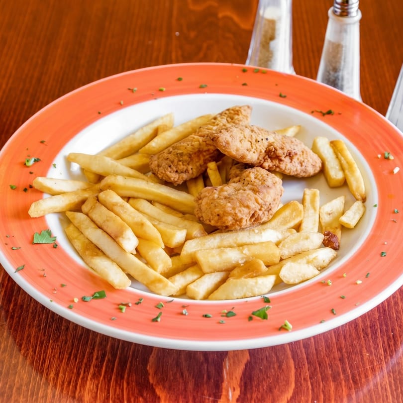 Crispy chicken tenders and golden french fries on a white plate with an orange rim.