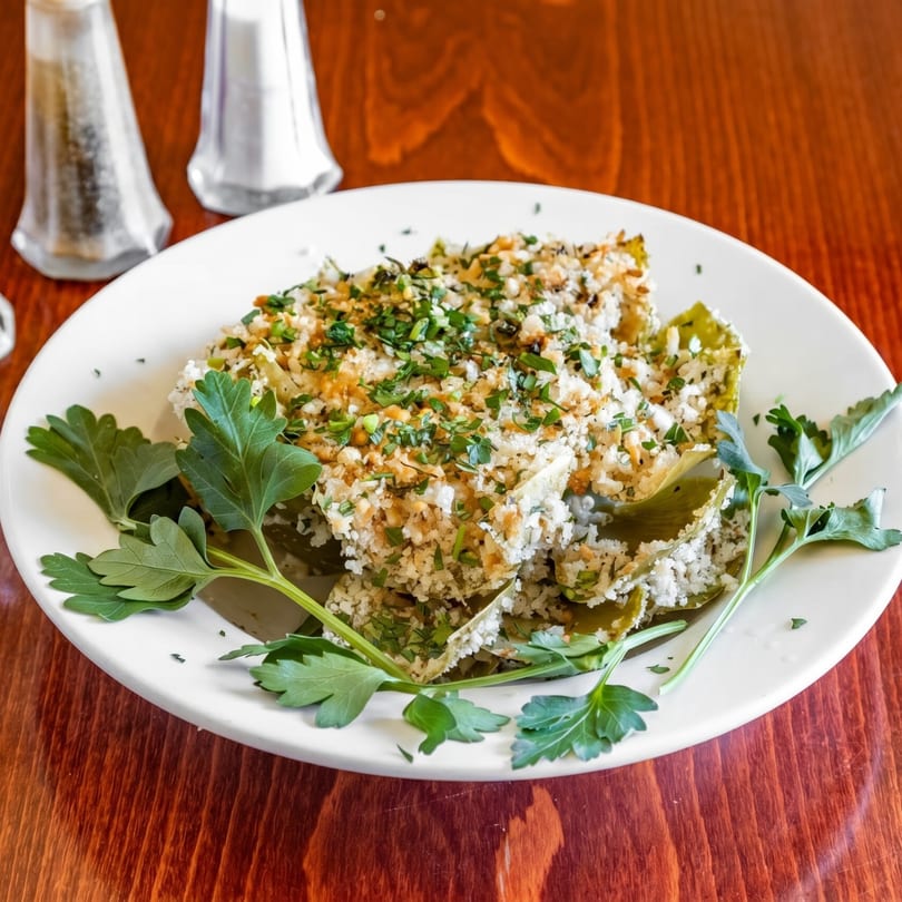 Baked artichoke hearts topped with breadcrumbs and fresh parsley, served on a white plate.